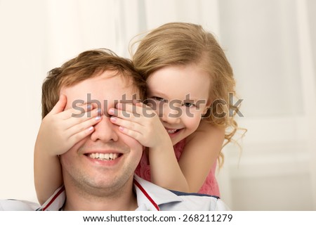 Father and daughter playing at home. Little girl closing dads eyes with hands and laughing. Family fun together