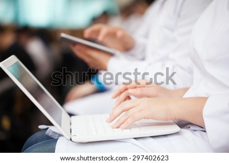 Woman and man doctors or medical students on the lecture or symposium. They using laptop and digital tablet. Focus on female hands typing on portable personal computer