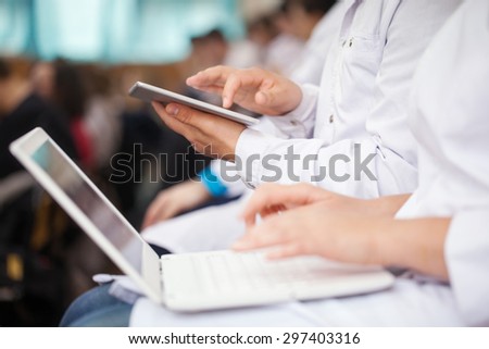 Male and female medical students or doctors using digital tablet and laptop during the lecture or conference. Focus on the man with pad
