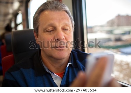 Mature man traveling with smart phone. He sitting by the window in train and looking at phone screen. Keeping in touch on the way