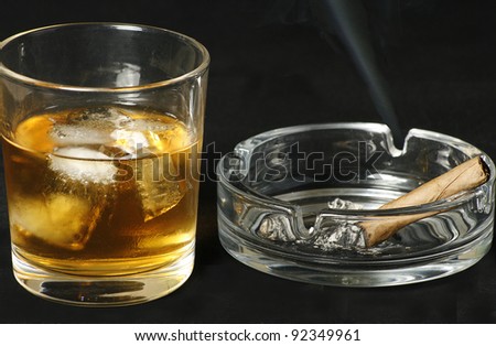 tumbler of scotch whisky with ice and a smoking cigar