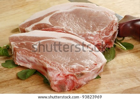 two uncooked pork chops on a wooden board