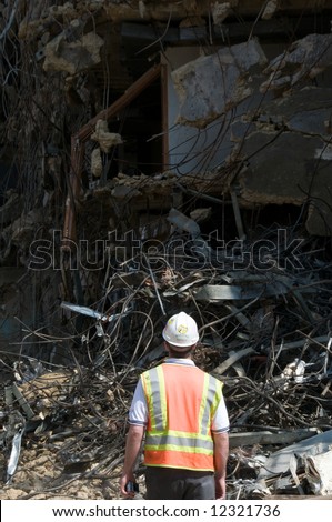 construction worker wearing hard hat and safety vest stares at the wreckage of a demolition project - selective lighting for more effective copyspace