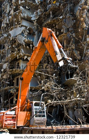 action shot of demolition equipment lifting scrap metal into a dumpster with a demolished building in the background