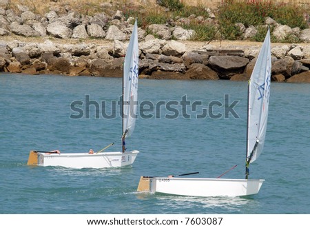 Two optimist class yachts sailing with their young sailors taking it easy
