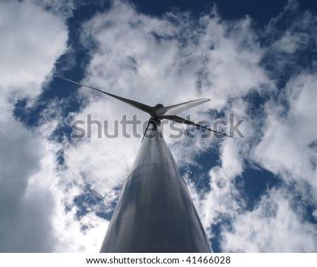 The height of a wind turbine tower backlit by the sun dwarfs the huge blades
