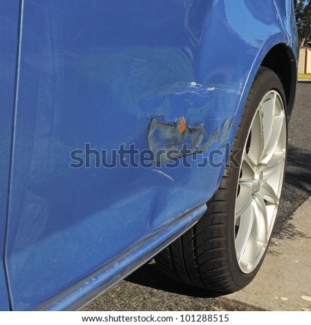 Damage on blue car door with bending, scratches and damaged paint after light road accident needs body repair, alloy wheel and asphalt in corner
