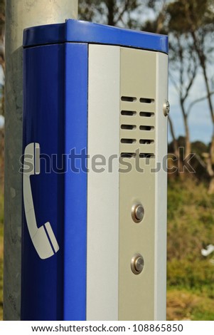 Public help phone on road as metal box with blue paint, phone sign and call buttons