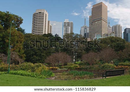 Colorful plants in Treasury Gardens, wooden bench, office building in background in Melbourne, Victoria, Australia