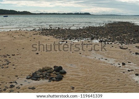 Black stones on beach with sand ripples clouds and calm water in Western Port Bay, Victoria, Australia