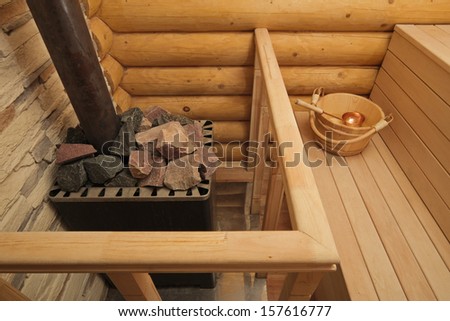 Wood-burning heater in traditional Russian log sauna with stones on top and bucket with spoon on wooden bench