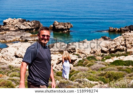 Smiling man and walking away blond in white dress on sea coast