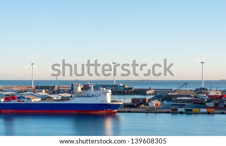 Cargo freight ship with crane at shipyard and wind electric generators on background