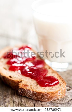 Bread with strawberry jam and glass of milk on wooden table