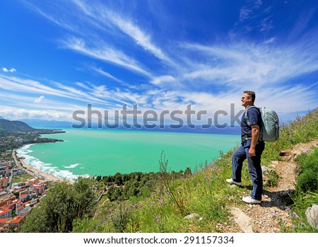 Smiling man with backpack looking at Cefalu city, Italy