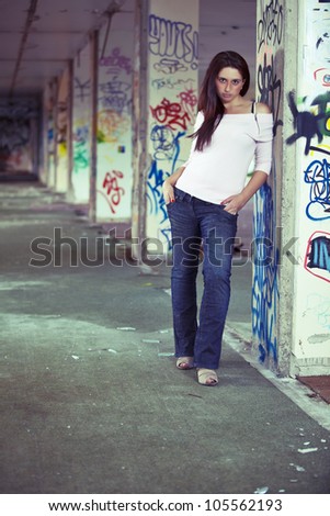 Young pretty long haired girl posing in abandoned graffiti painted building. With channel mixing effect