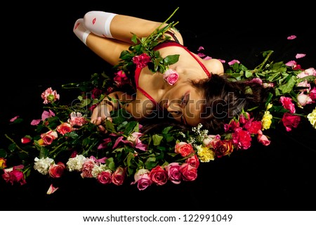 Young sexy girl wearing red lingerie posing laying on flowers. Studio low key shot