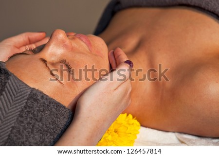 Beautiful young woman getting facial massage at spa salon. Dim light. Close-up