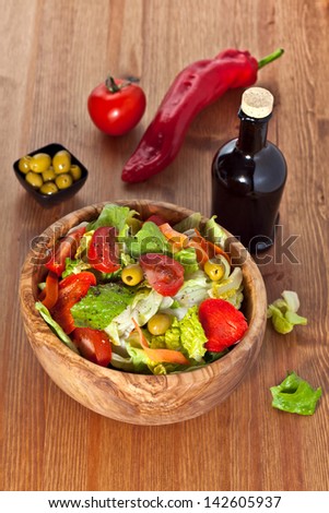 Bowl made of olive wood filled with cos and iceberg lettuce salad with paprika, carrots, tomatoes and green olives on wooden table. More healthy food in my portfolio