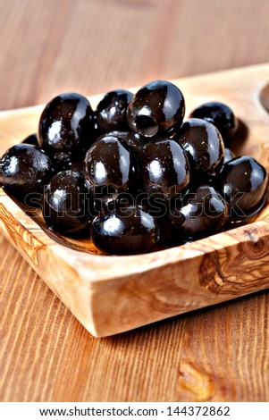 Closeup of Black pitted marinated olives in olive tree dish on wooden table