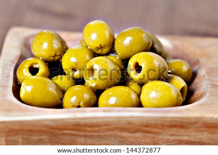 Closeup of Green pitted marinated olives in olive tree dish on wooden table