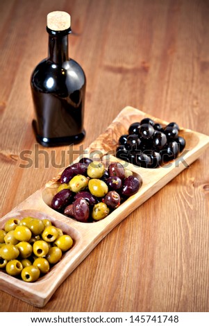 Variety of green, black and mixed marinated olives in olive tree dish on wooden table and a bottle of extra virgin olive oil