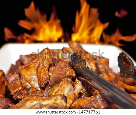 Heap of grilled roasted meat pork or chicken chunks on plate with fire flame on background