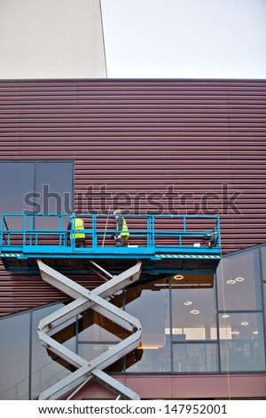 Builder on a Scissor Lift Platform at a construction site. Men at work