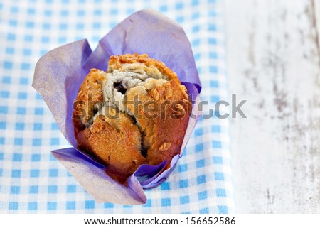 Homemade blueberry muffin wrapped in paper on blue checkered cloth. Top point of view