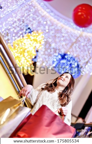 Beautiful young woman in white knitted sweater and blue jeans posing with shopping bags in mall during the Christmas sale.