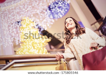 Beautiful young woman in white knitted sweater and blue jeans posing with shopping bags in mall during the Christmas sale.