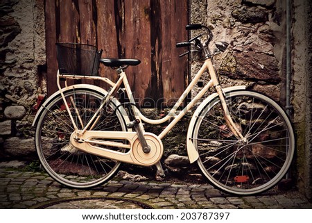 Italian old-style vintage yellow bicycle with the basket standing against a grunge wall under a wooden door
