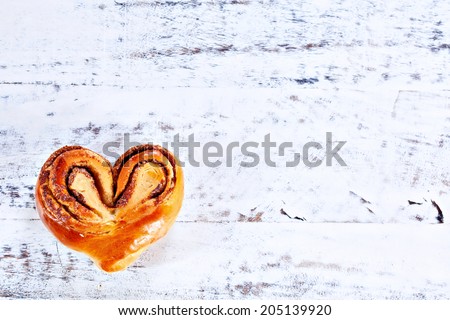 Rustic home-made heart shape cinnamon roll on white painted board or table. Copy-space place for your text