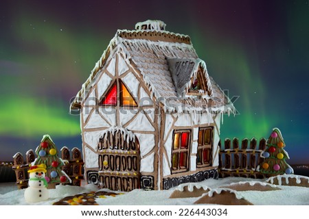 Decorative gingerbread house with lights inside with Northern lights on background. Rural Christmas night scene