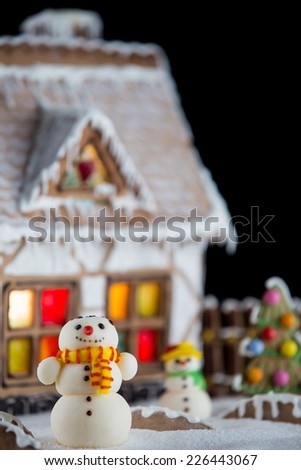 Decorative snowmen and gingerbread house with lights inside on black background. Rural Christmas night scene