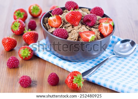 Bran flakes with fresh raspberries and strawberries on blue checkered cloth. Healthy eating choice concept