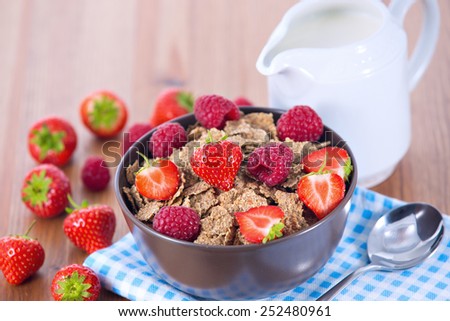 Bran flakes with fresh raspberries and strawberries on blue checkered cloth and a pitcher of milk. Healthy eating choice concept
