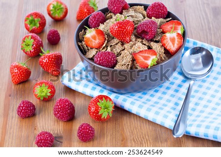 Bran flakes with fresh raspberries and strawberries on blue checkered cloth. Healthy eating choice concept