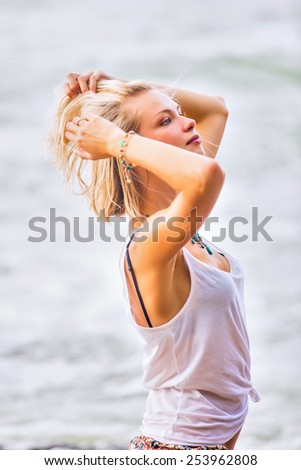 Beautiful young blonde woman posing outdoor at the rocky sea shore. Trendy fashion female model dressed in white top