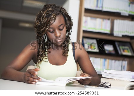 Pretty teenage black african college student girl studying and reading a book in college library