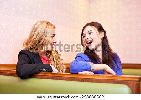 Two young pretty caucasian girls with long hair chatting and having fun at a cafe