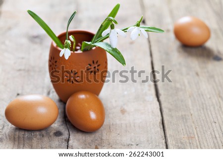 Easter bunch of snowdrop flowers in clay vase and eggs on wooden floor.