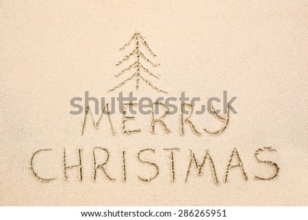 Merry Christmas inscription on wet yellow shoreline beach sand. Holiday wish message