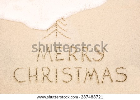 Merry Christmas inscription on wet yellow shoreline beach sand. Holiday wish message
