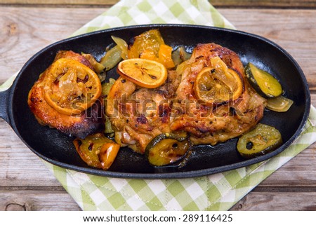 Delicious baked chicken thighs with lemon slices, onion and zucchini served in cast-iron frying pan on rustic wooden table above view