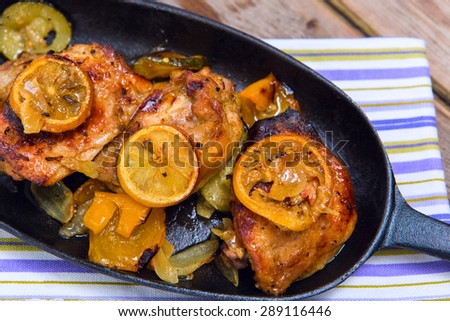 Delicious baked chicken thighs with lemon slices, onion and zucchini served in cast-iron frying pan on rustic wooden table above view
