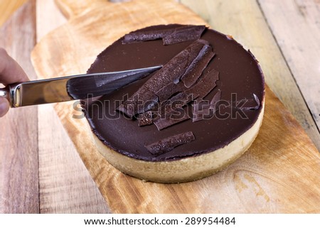 Fresh classic homemade Cheesecake with dark chocolate topping on wooden board and vintage table knife aside