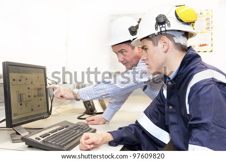 Senior and junior engineers discussing work together in office, senior man pointing at screen