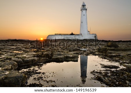 Reflected St Marys Lighthouse at sunset / The sun goes down behind St Marys Island reflecting the lighthouse in a rockpool