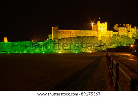 Bamburgh Castle at night with fence / Bamburgh Castle at night illuminated by green and golden lights
